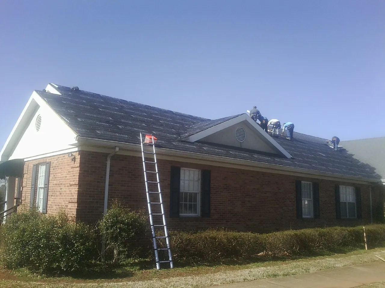 Crew tearing shingles off a brick ranch roof with a ladder set — Emergency Roof Repair work by our crew in Battle Creek
