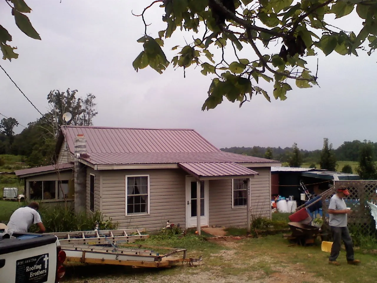 Crew finishing a mauve metal roof on a small farmhouse in Battle Creek