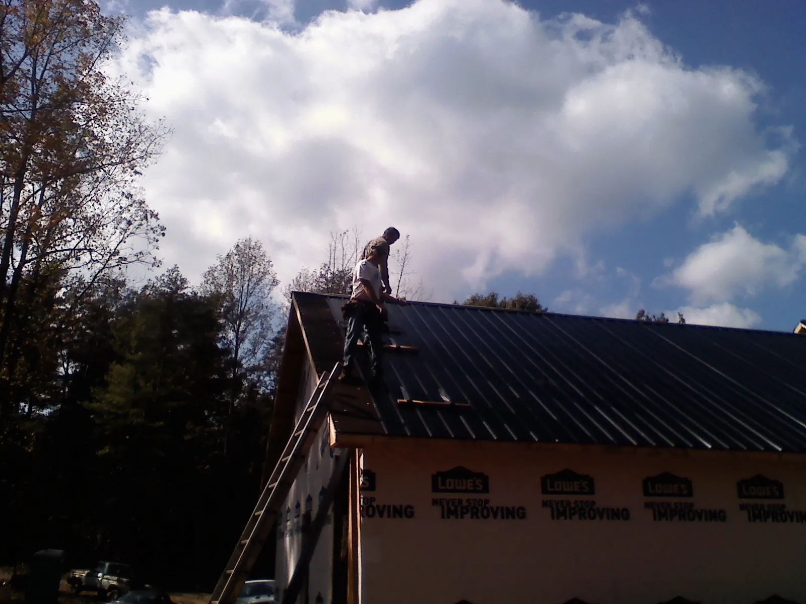 Roofer fastening dark metal panels high against a cloudy sky, from a Roof Inspection job in Battle Creek